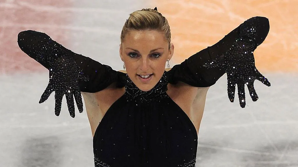 Jenna McCorkell has her blonde hair in a bun. She is wearing a black sequined top and long gloves.  