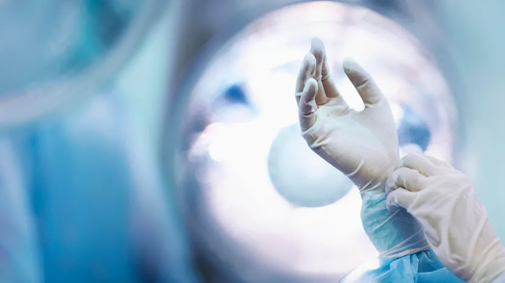 Surgeon adjusting glove in operating room.