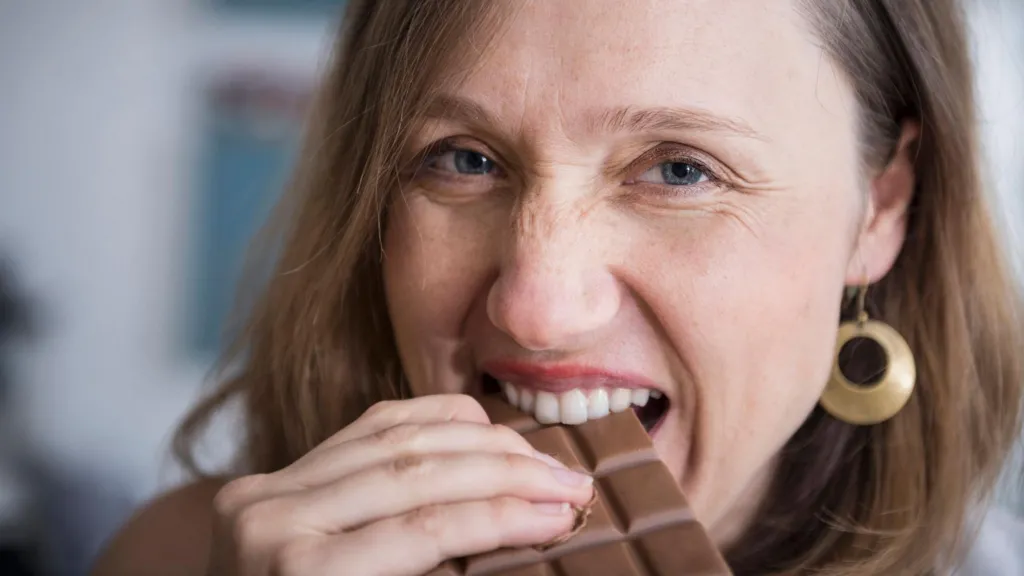 A woman takes a bite from a big bar of chocolate