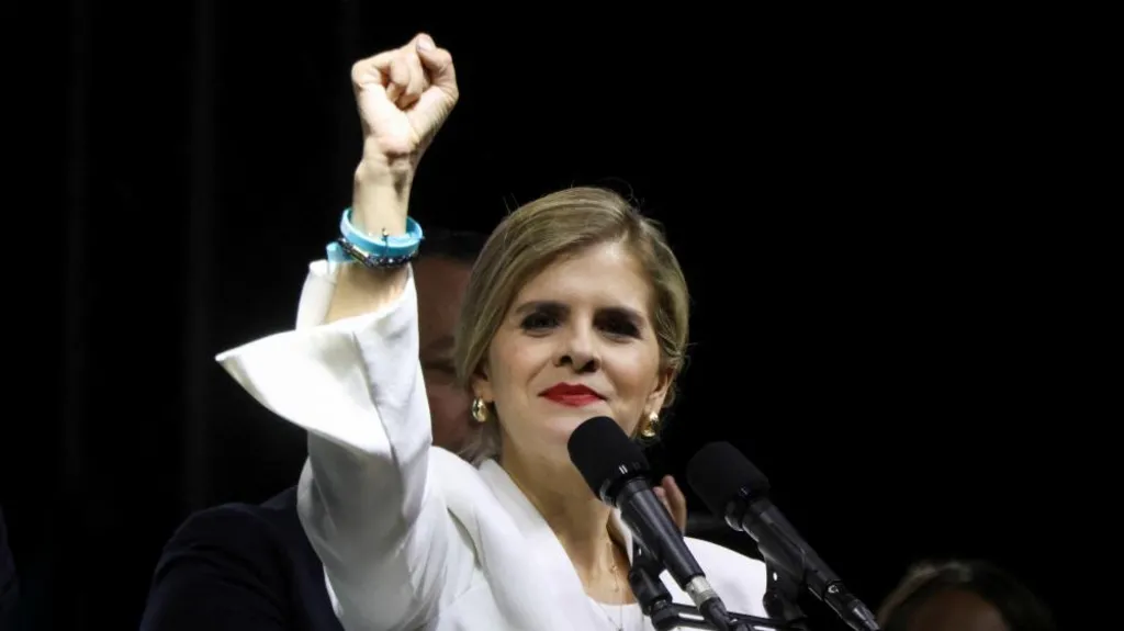 Presidential candidate Laura Fernandez of the Sovereign People's Party holds up her right fist in a gesture of triumph as preliminary results give her an insurmountable lead in the presidential election. She is wearing a white jacket, red lipstick and gold earrings. She is standing in front of microphones at a reallt in San Jose, Costa Rica, on 1 February, 2026. 