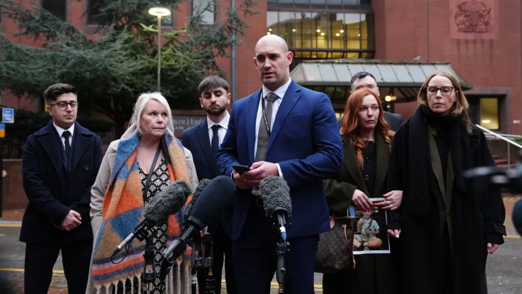 Detective Inspector Joe Davenport stands with members of Leo Ross' foster family outside Birmingham Crown Court. There are three women dressed in winter coats stood with four men in dark clothing outside the court. Their faces are sullen as Davenport speaks to the media. The court can be seen behind the group.