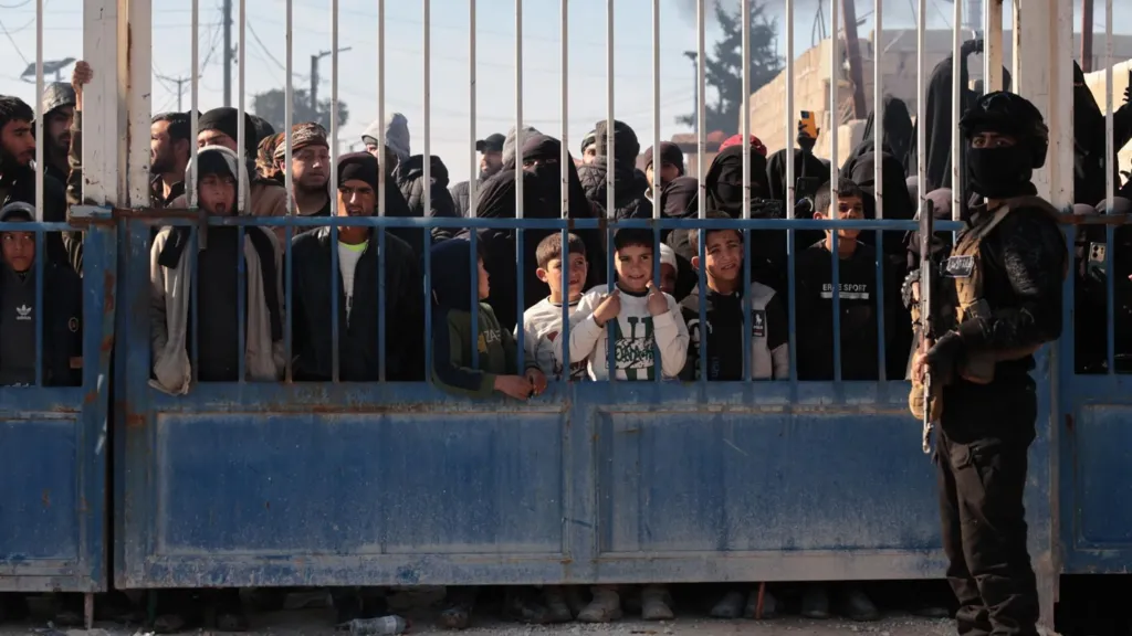 Syrian security forces stand in front of the gate of the al-Hol camp, behind which stand family members of suspected IS members, in Hassakeh province, Syria (21 January 2026)