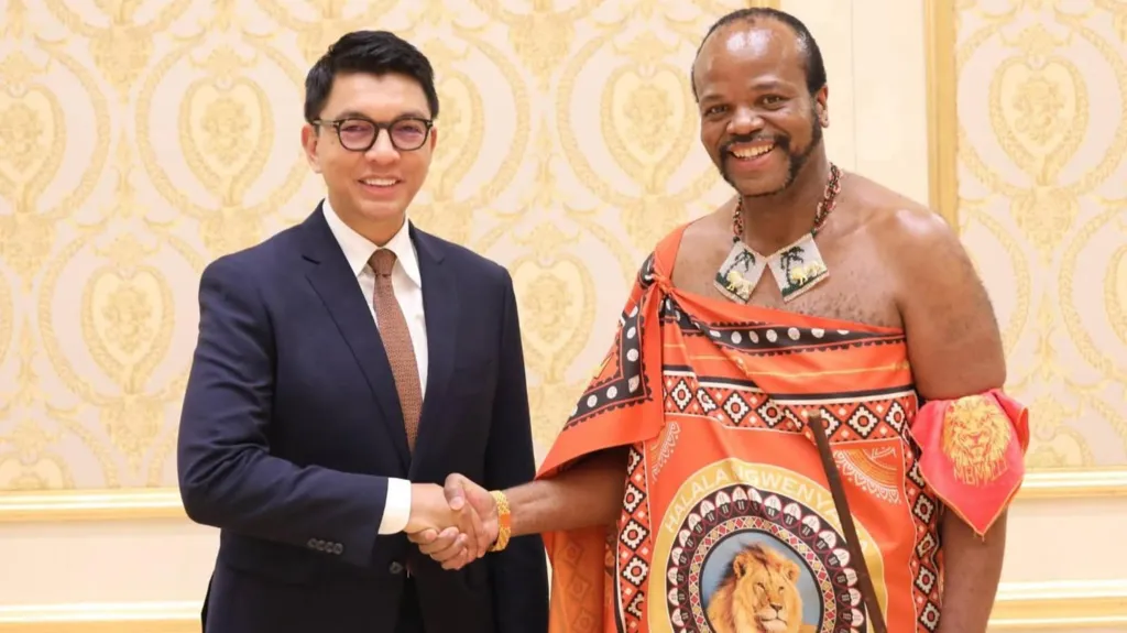 King Mswati III, dressed in traditional Eswatini attire, shake hands with Andry Rajoelina, who is wearing a suit and tie.