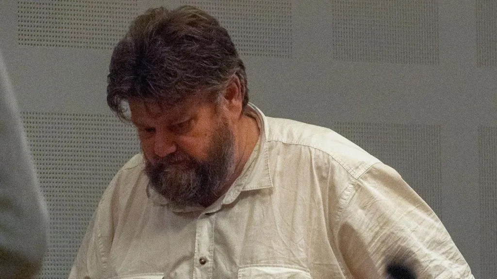 Carl Beech, a man in his 50s with dark grey hair and a mid-length beard, walking along with his head down, wearing a cream-coloured shirt.