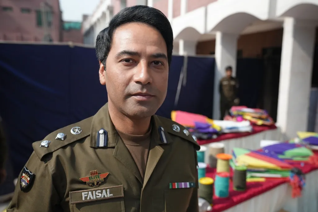 Faisal Kamran in his police uniform stands in front of a brightly coloured table which is lined with confiscated kites and rolls of string