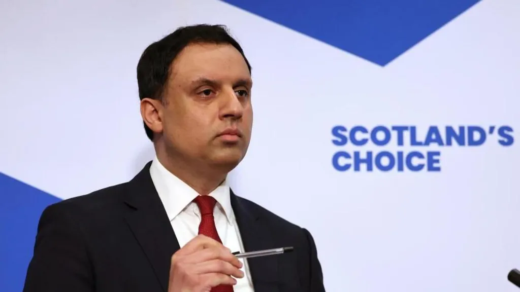 A man in suit and tie speaks to reporters.