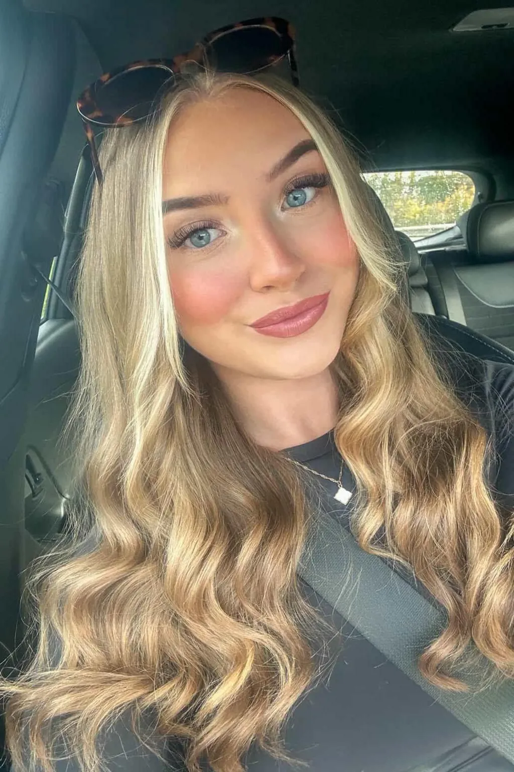 A selfie of Lily-May without her glasses. She wear dark sunglasses on top of her head. She has blue eyes and pink lipstick