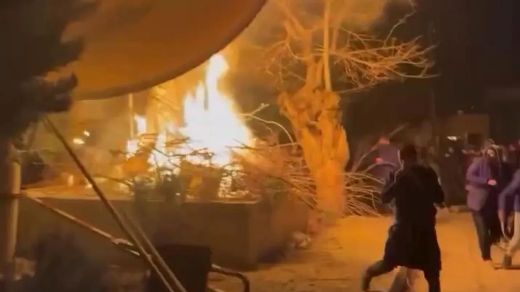 Screenshot from phone footage, showing a satellite dish on fire with some people running past