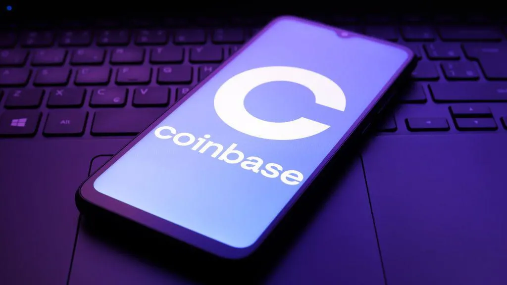 Coinbase's logo displayed on a smartphone screen. The handset is lying on top of an illuminated laptop keyboard.