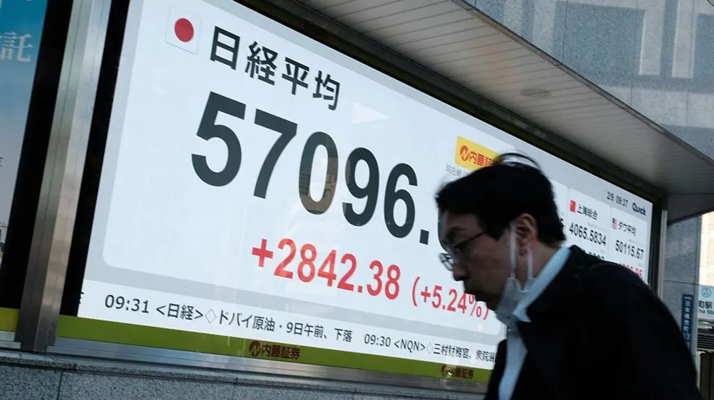 A man walks in front of a giant screen showing the Nikkei Index at 57,096