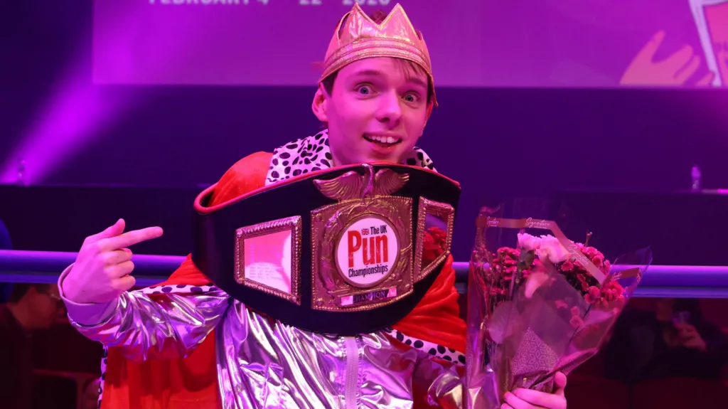 Adam Ernest Pickard bathed in purple light with a boxing-style belt around his shoulders