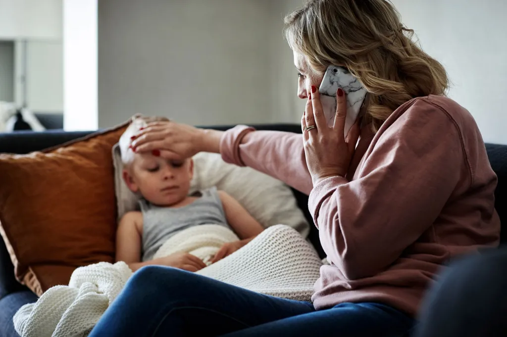 Woman and child o a sofa. The woman is on the phone while touching the forehead of the child, who looks ill