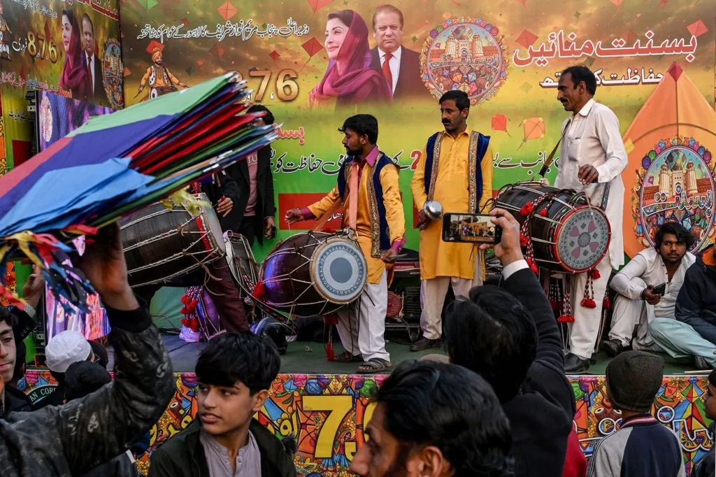 Artists play traditional drums next to a hoarding with portraits of Pakistan's former Prime Minister and leader of the Pakistan Muslim League Nawaz (PMLN) party Nawaz Sharif and his daughter and Chief Minister of the country's Punjab province Maryam Nawaz Sharif, as vendors sell kites to mark Basant Festival in Lahore on February 4, 2026.