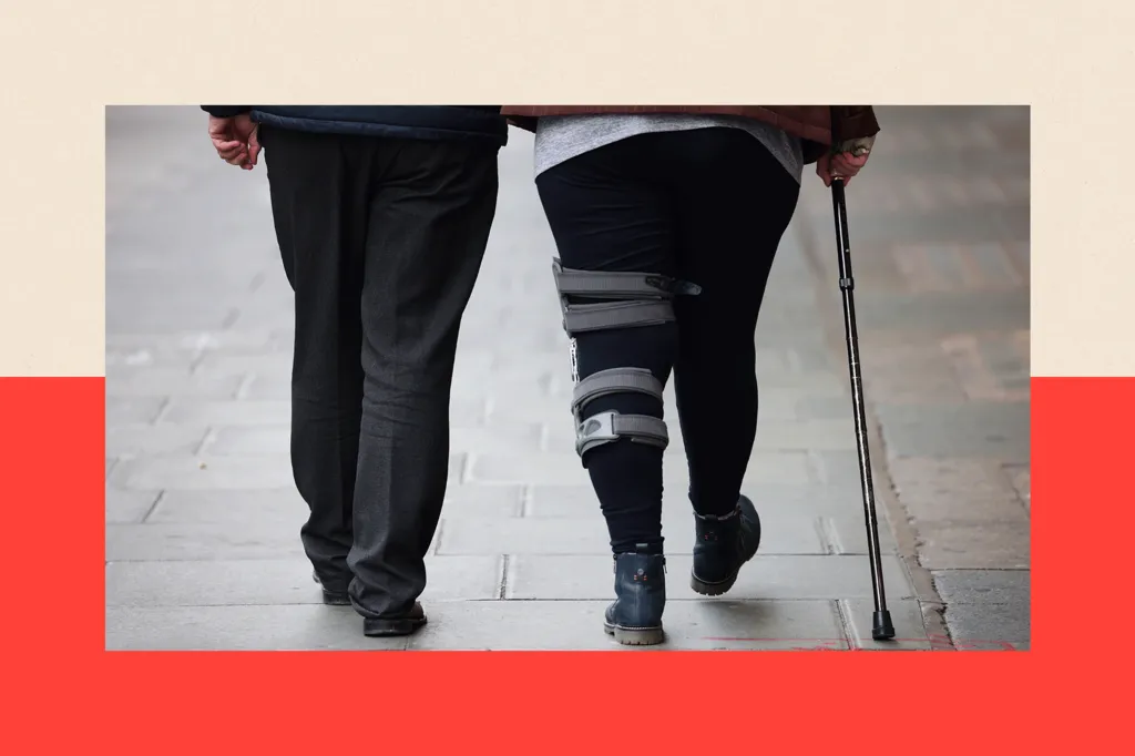 A woman with a leg brace and a walking stick walks alongside a man, only the bottom half of their legs showing
