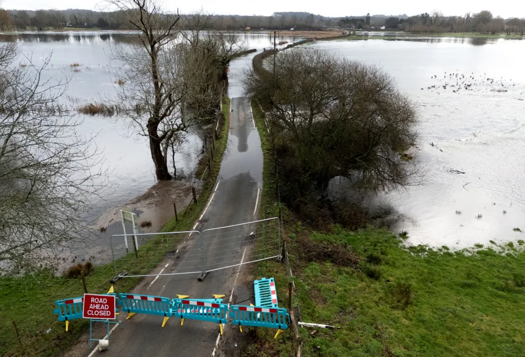 A 'road closed ahead' sign and green barriers block a road flooded with high waters on either side of it near to Harbridge in Hampshire, taken on Friday.