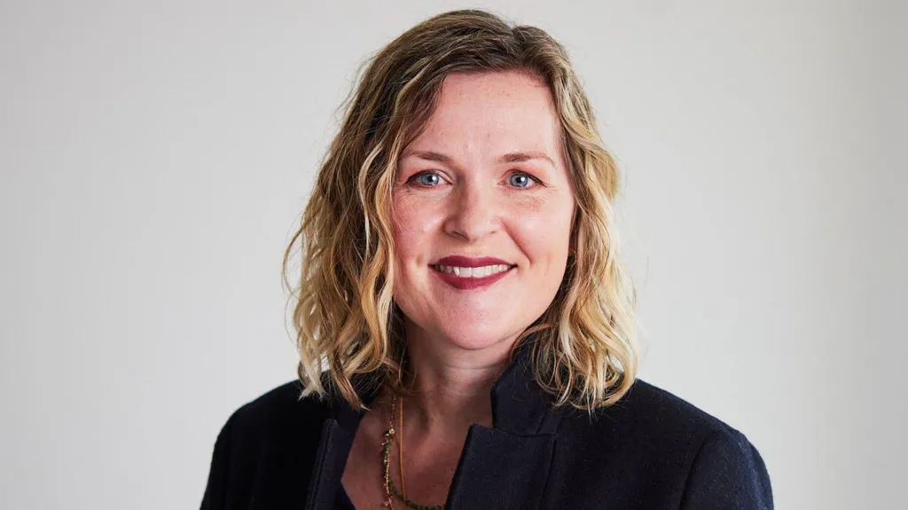 Headshot of Claire McCartney. She has blue eyes, wears red lipstick, and has shoulder-length blonde hair with brown roots