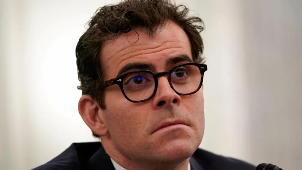 Adam Mosseri, head of Instagram, speaking before a Senate committee in 2021 wearing rounded black-rimmed eyeglasses and a simple dark blue suit and tie. 