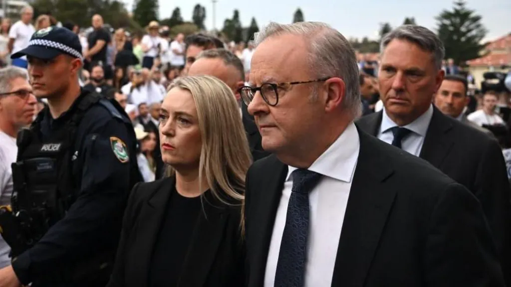 A grey-haired man in a dark suit and tie and a blond haired woman in dark clothing in a crowd of people.