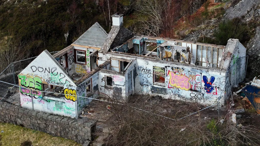 An aerial view of the ruined, vandalised cottage showing the roof removed.