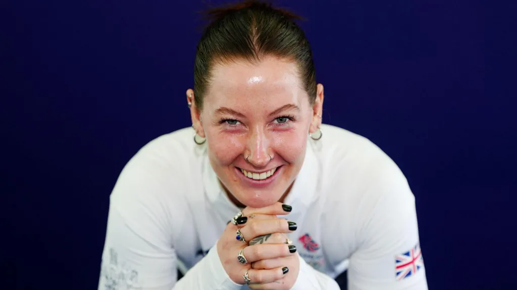 Makayla Gerken Schofield pictured in a Team GB publicity shoot. She is wearing a white long-sleeved top and is leaning on their hands. She has dark hair pulled back and is smiling.