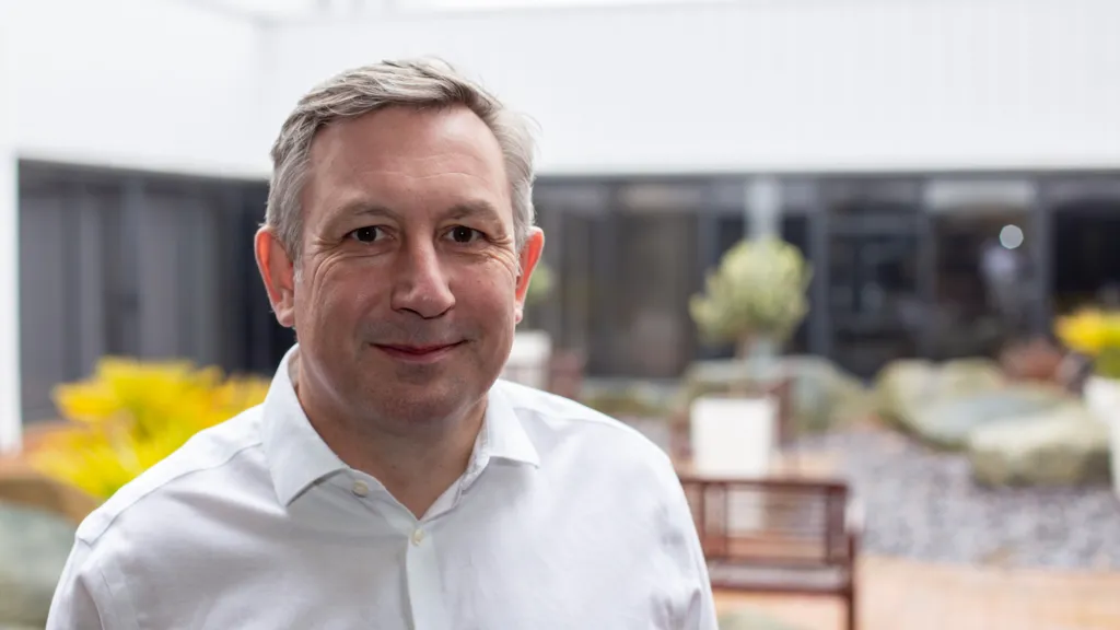 Wearing a smart, white shirt, Nick Rutter smiles at the camera.