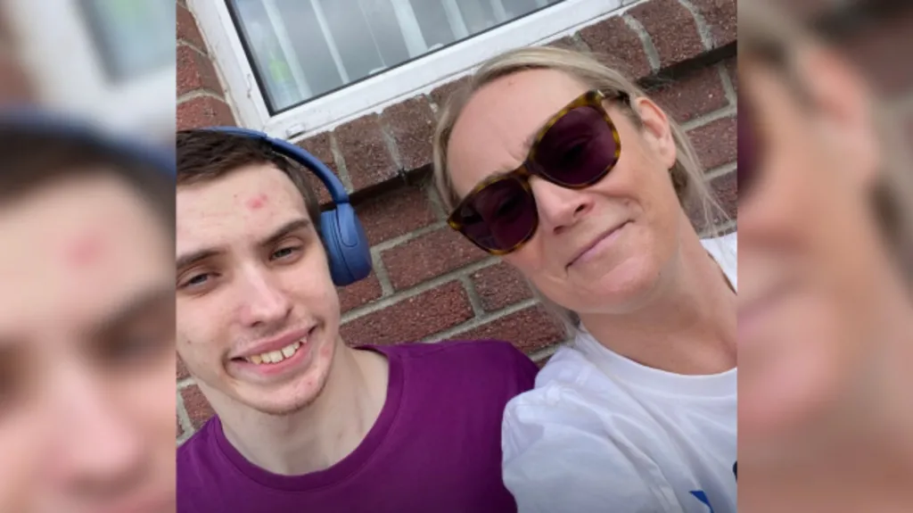 A young boy with short dark hair is sitting next to his mum who has blonde hair tied back. He has blue headphones on his head and a purple t-shirt, while she is wearing sunglasses and a white t-shirt.