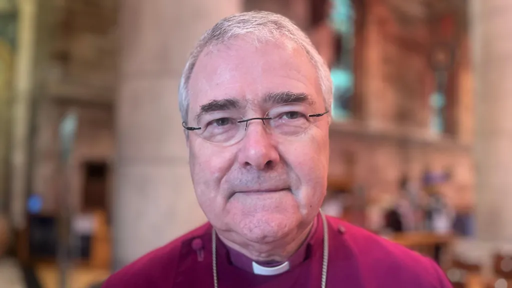 The Archbishop of Armagh, the Most Rev John McDowell is looking at the camera. He is wearing glasses and has short white/grey hair. He has a red coloured robe on.