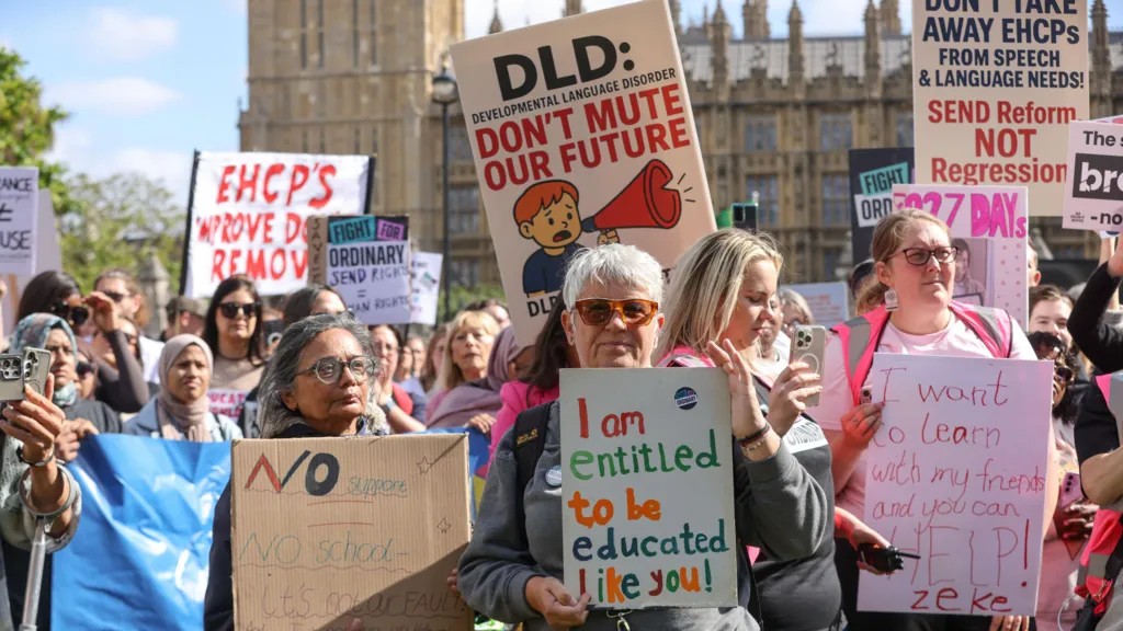 People are standing outside Westminster on a sunny day with placards protesting. They are holding signs regarding Send such as "I am entitled to be educated like you" and "I want to learn with my friends and you can help"