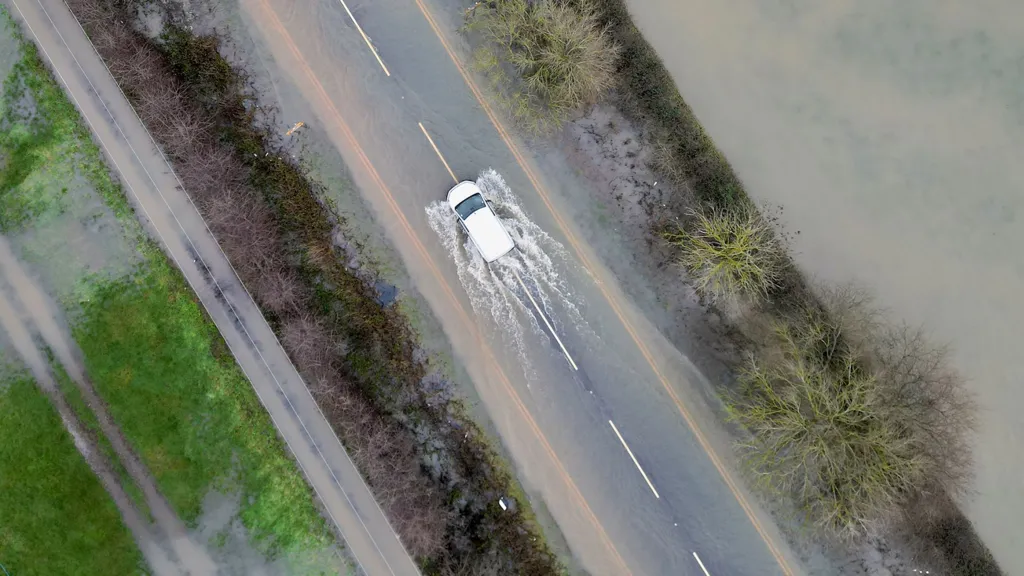 An aerial view shows a white car driving down a road with floodwater in the road and beside it, in Leicestershire on Monday.