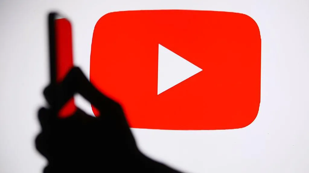 A silhouetted hand holding a smartphone in front of a background of YouTube's red and white logo.