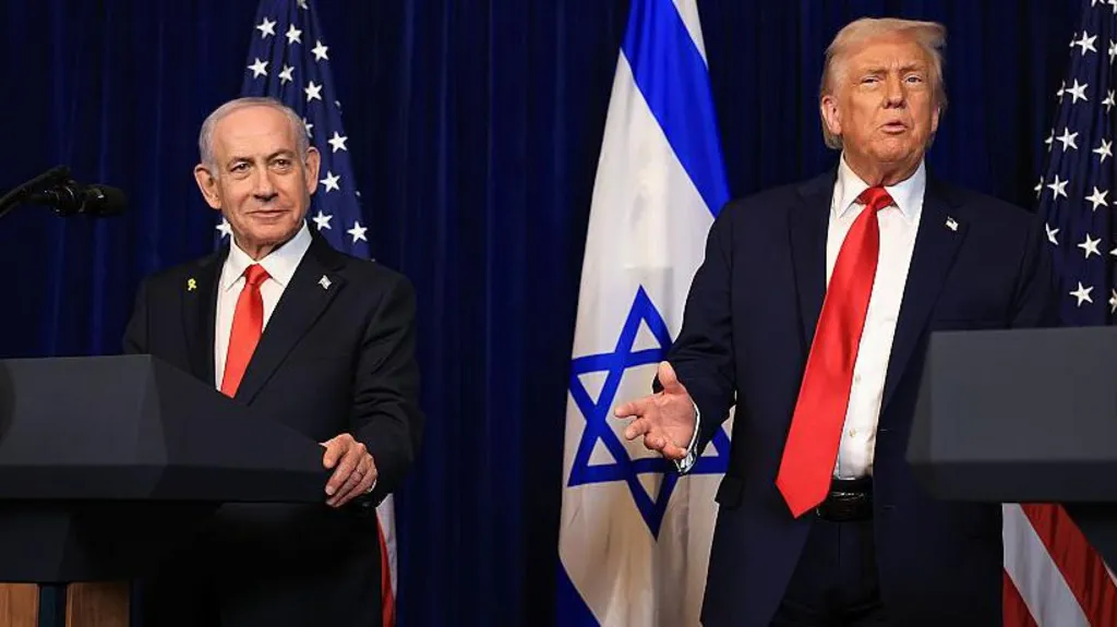 A smiling Netanyahu, who has grey hair and wears a suit, at a lectern in during a press conference at Mar-a-Lago in December with Trump, who has blonde combed over hair and also wears a suit