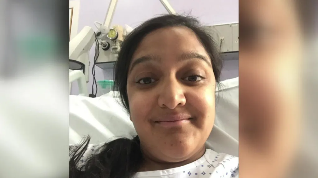Sanju Pal, with her black hair tied in a ponytail smiles, into the camera from her hospital bed