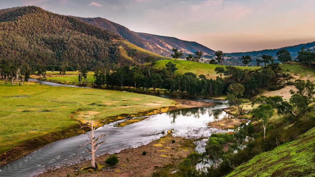 A view of a river at sunset with green lush trees lining its banks and mountains in the background