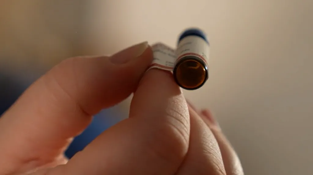 The picture shows only the right hand of Dr Caroline Copeland who holds between her index finger and thumb, a vial the size of the tip of her finger, containing nitazene with a laboratory label wrapped around it