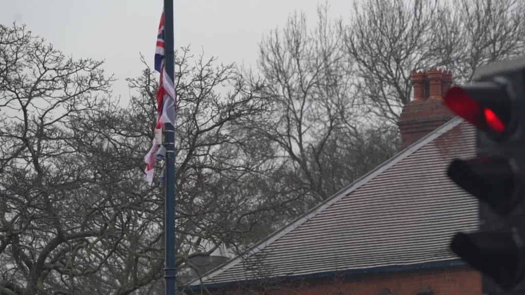 A union jack is attached to a flag pole. A sloping roof can be seen on the right with a traffic light in the foreground