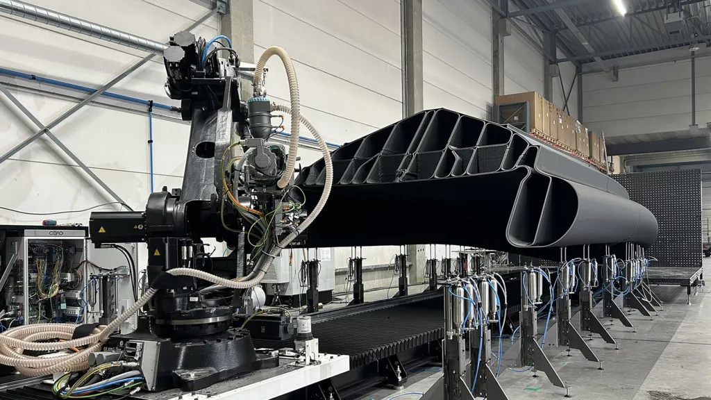 A robotic arm with a 3D printer works on a nearly completed boat hull.