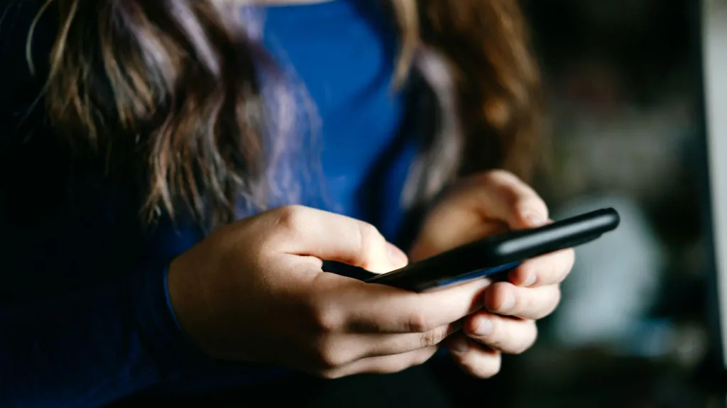 A focused view of a young woman's hands holding a mobile phone indoors.