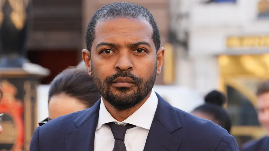 Noel Clarke in a dark suit outside court
