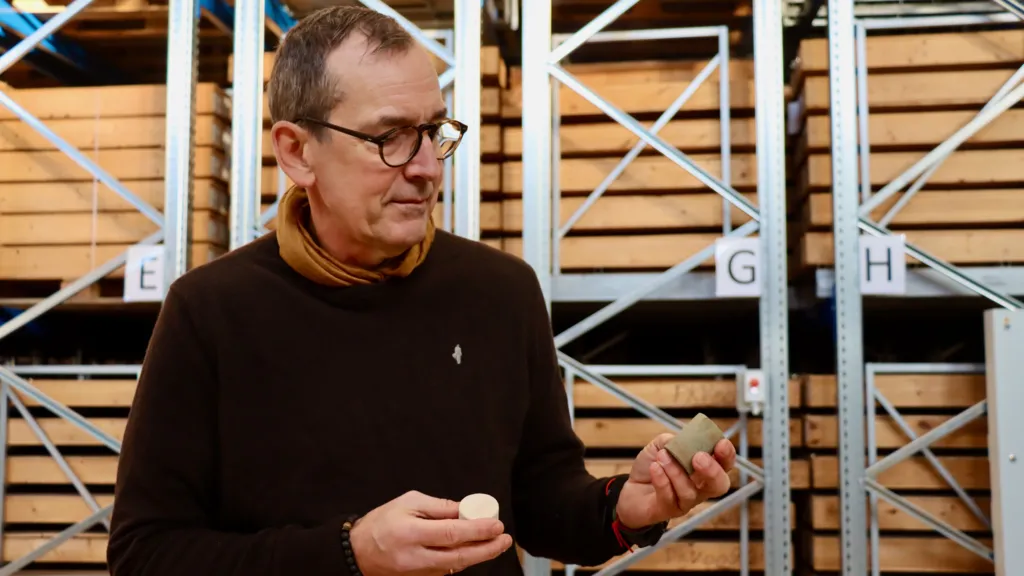 Niels Schovsbo, wearing a black jumper and scarf, examines rock samples in a warehouse.