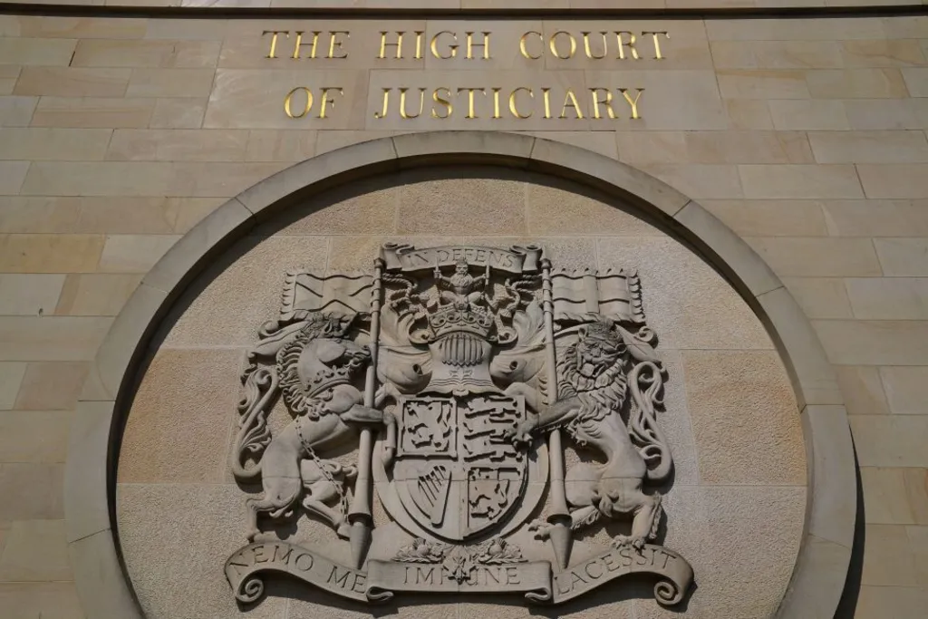 The wall of a sandstone building with a crest. Gold letters above it read "THE HIGH COURT OF JUSTICIARY"