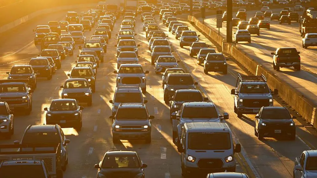 A freeway crowded with lines of cars, many with headlamps on, all bathed in the orange light of early morning in Los Angeles