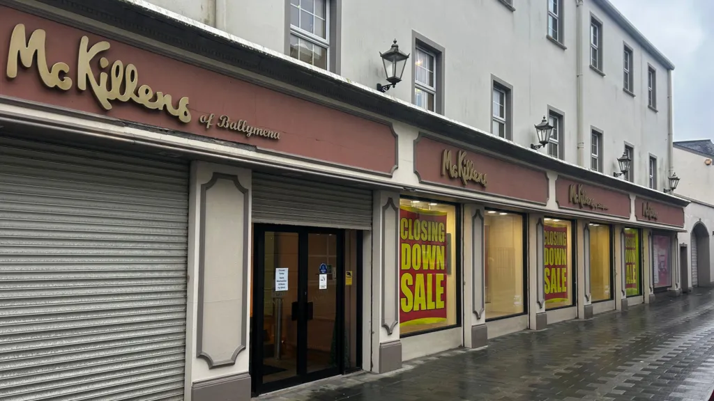 McKillen's store front with CLOSING DOWN SALE on all the windows in yellow and red. The shop front is grey with a brown/red sign and in gold writing McKillens of Ballymena.