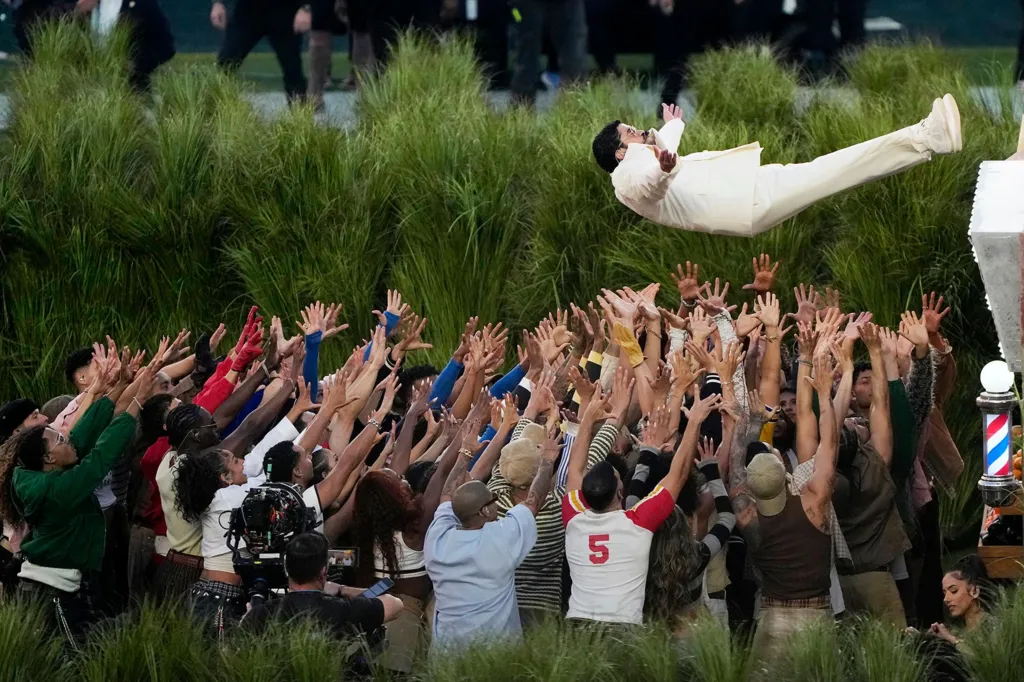 Bad Bunny falls backward from a platform into a crowd of dancers holding up their hands to catch him as he performs at halftime in Super Bowl LX 