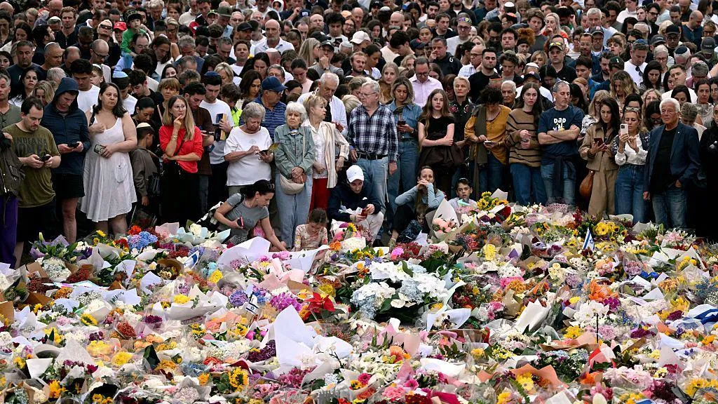 Mourners gather in front of a sea of floral tributes at a makeshift memorial at the Bondi Pavilion in memory of the victims of a shooting at Bondi Beach