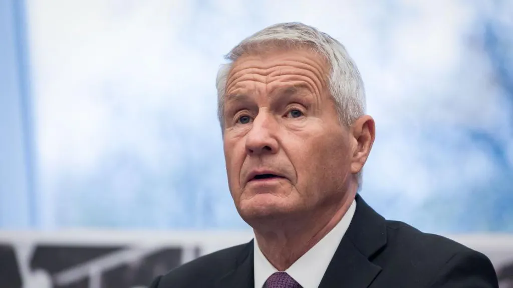 Former Norwegian Prime Minister Thorbjørn Jagland dressed in a black suit jacket, white shirt and a purple tie, he looks off to the left, his mouth tilted down. His hair is grey and skin tanned. The background is blurred. 