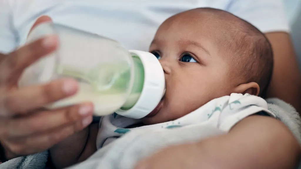 Stock photo shows a baby being held and fed with a formula milk bottle.