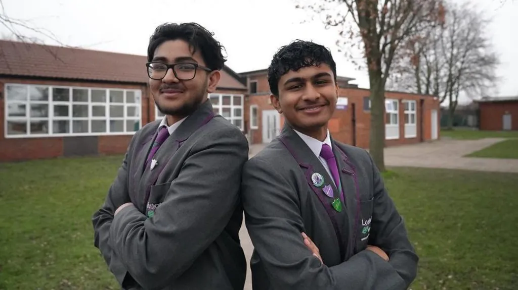 Abdullah and Bakhtiar are standing back to back with their arms folded smiling at the camera. They are wearing their gray school blazers, purple ties and white shirts. 