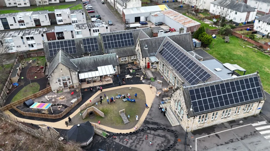 A drone image of a school with children playing in the centre, surrounding by buildings with solar panels on the roof.