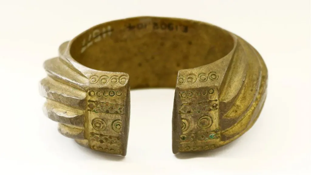A brass penannular bracelet decorated with heavy slanting bands