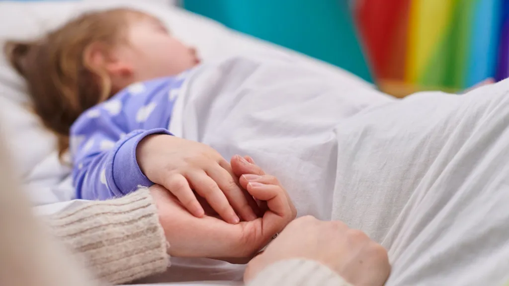 Child in hospital bed with parent holding hand